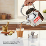 Load image into Gallery viewer, Hand pouring hot chai tea from stainless steel Max Fresh tea kettle into glass cup on white countertop with spices