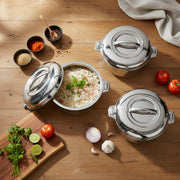 Set of three stainless steel pots on wooden table with cooked rice, spices, tomatoes, garlic, lime, and herbs