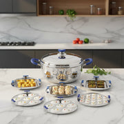 Stainless steel idli maker set with blue handles, filled with idlis and snacks on marble countertop