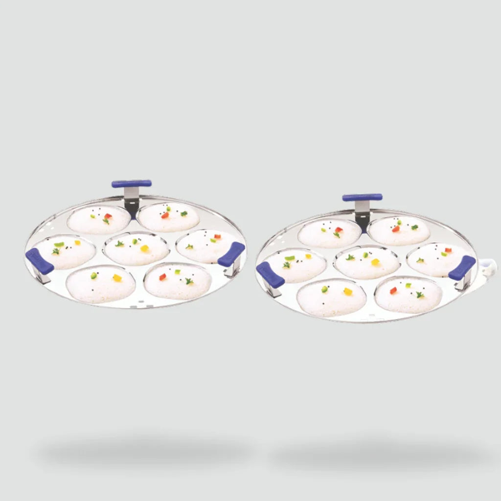 Stainless steel idli plates with blue handles, holding steamed idlis, on a light background.