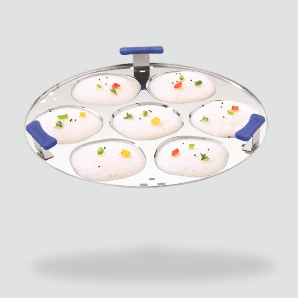 Stainless steel idli plate with six steamed idlis, blue handles, isolated on grey background