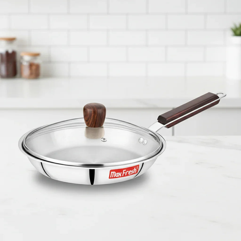 Stainless steel frypan with glass lid and wooden handle on a kitchen countertop