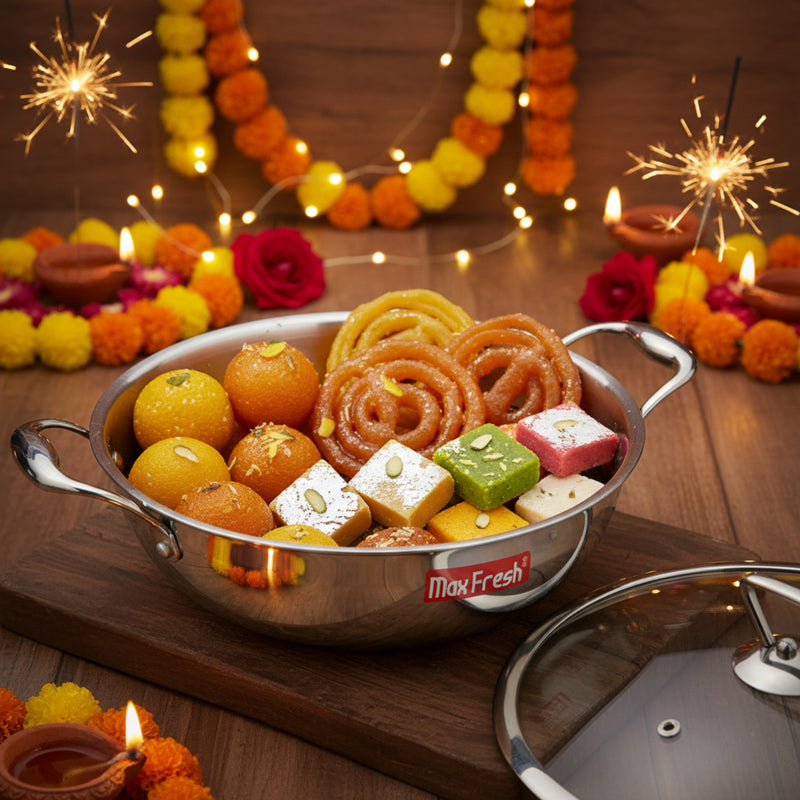 Assorted sweets in a metal bowl with Diwali decorations including lights and sparklers on a wooden surface.