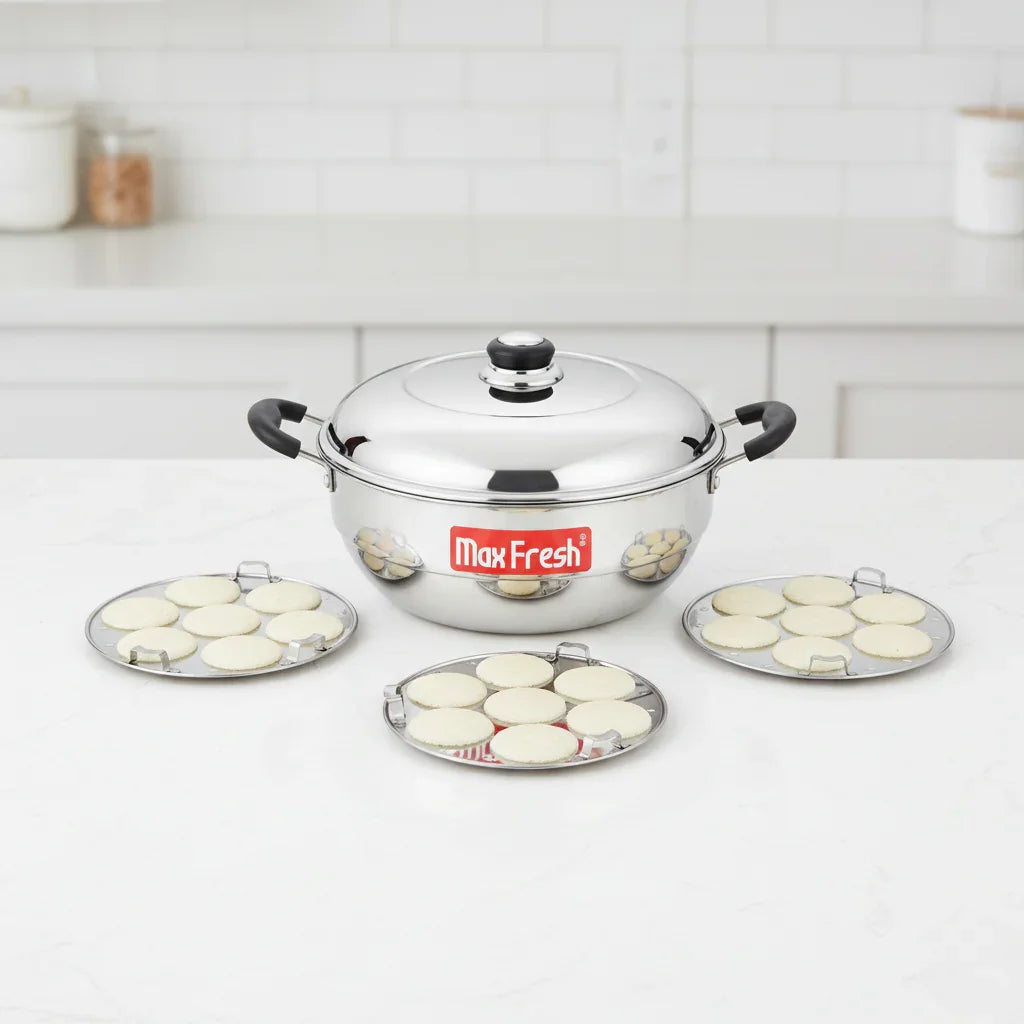 Stainless steel idli cooker with three idli plates, each holding steamed idlis on a kitchen counter.