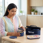 Woman opening insulated lunch box with stainless steel containers and cooked meal inside modern kitchen