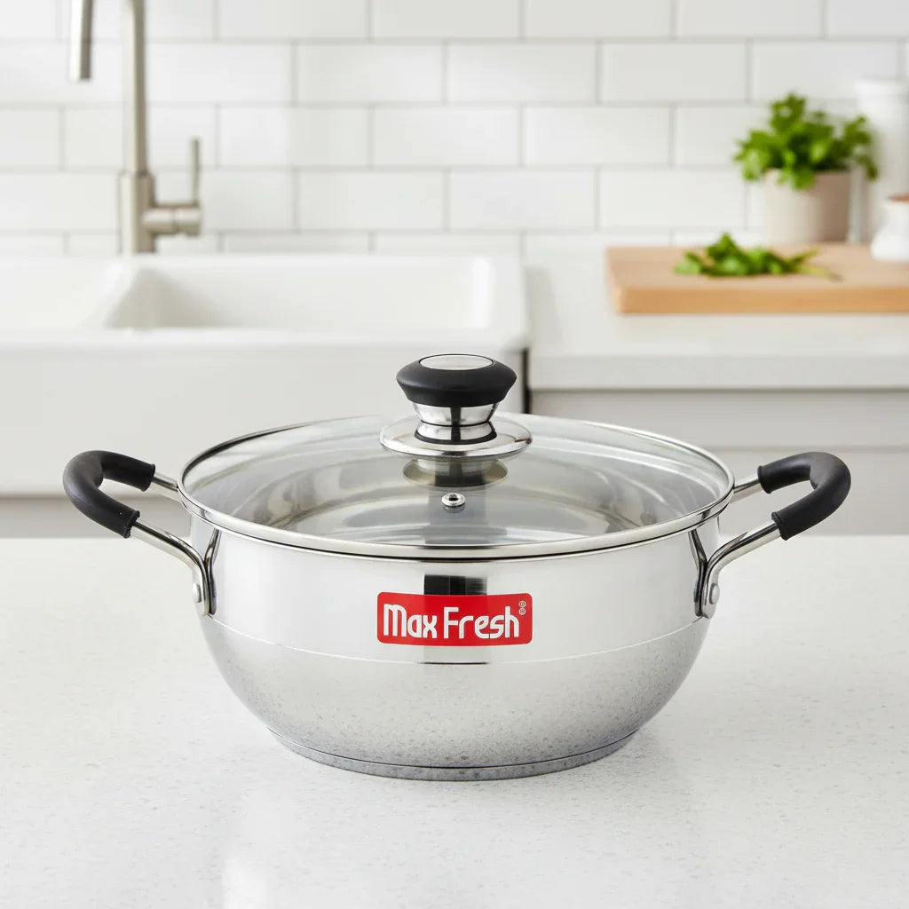 Stainless steel multi kadai with glass lid and black handles on a kitchen countertop