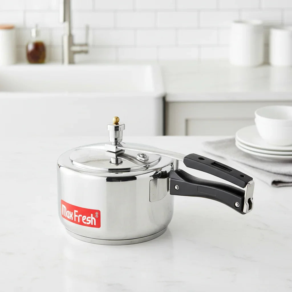 Stainless steel pressure cooker with black handles on a white kitchen countertop