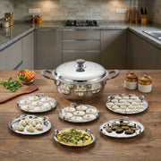 Stainless steel multi-kadai with six plates holding various Indian snacks on a wooden kitchen counter