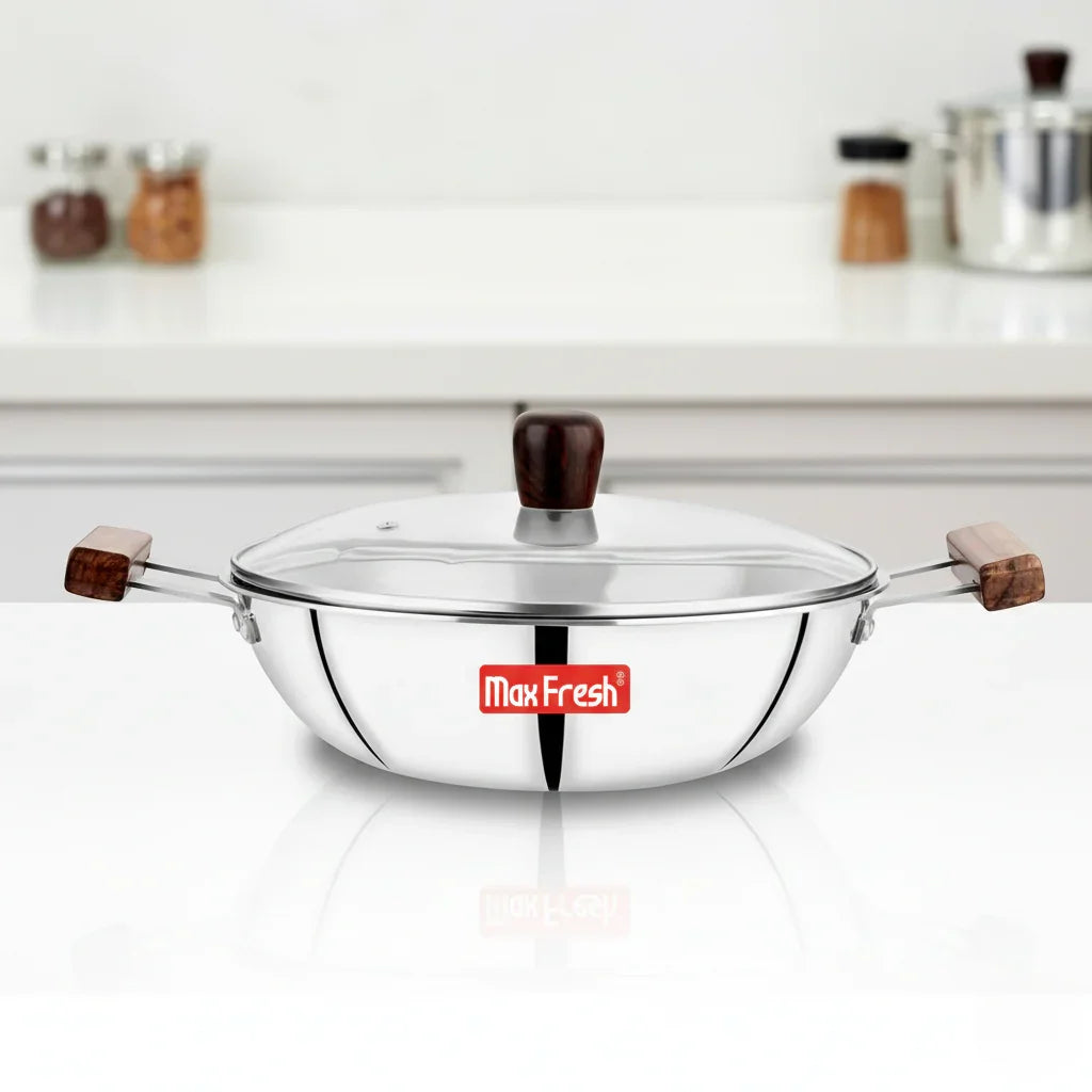 Stainless steel triply kadai with glass lid and wooden handles on a kitchen counter