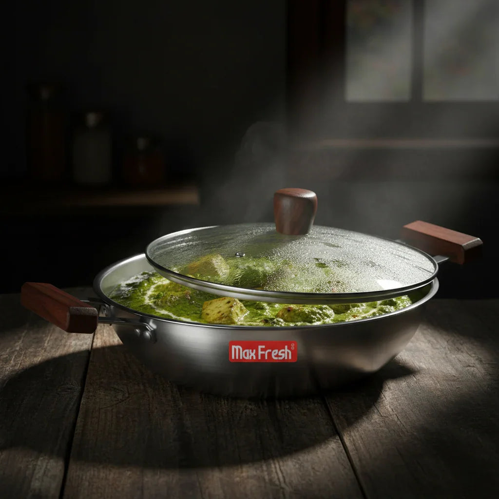 Steaming stainless steel triply kadai with glass lid and wooden handles on kitchen table