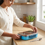 Woman sealing a blue stainless steel lunch box with airtight lid on kitchen counter