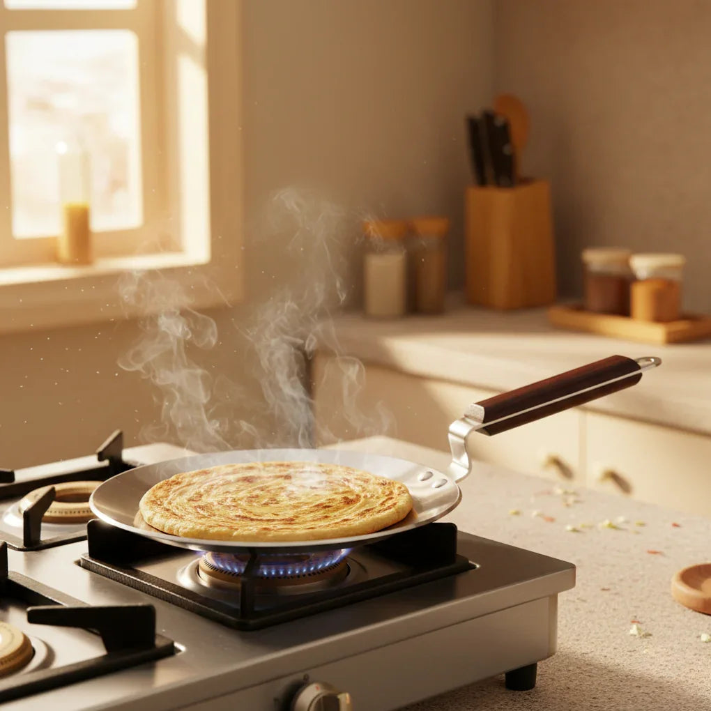 Stainless steel tawa with wooden handle cooking flatbread on a gas stove with steam rising in bright kitchen