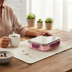 Stainless steel lunch box with pink lid on table beside coffee and oatmeal, cozy kitchen setting