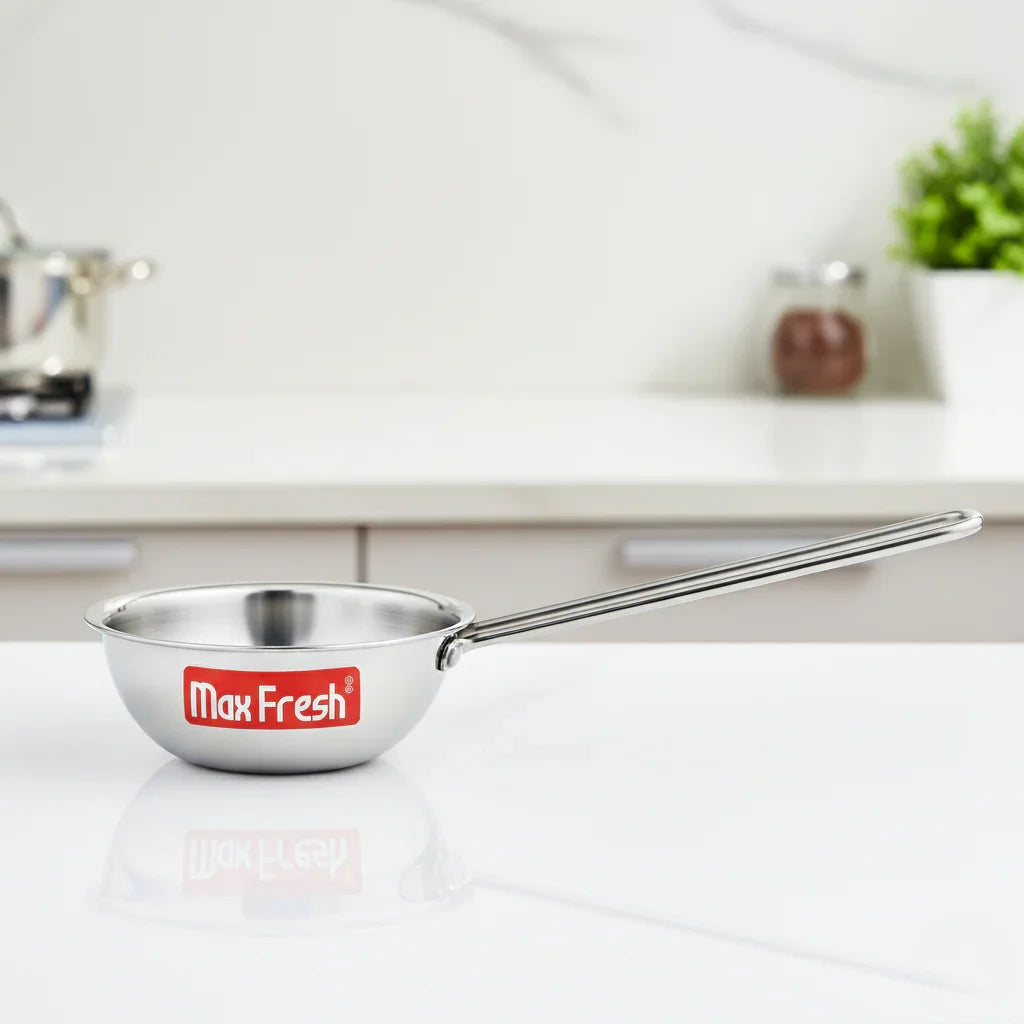 Stainless steel tadka pan with long handle on a modern kitchen countertop