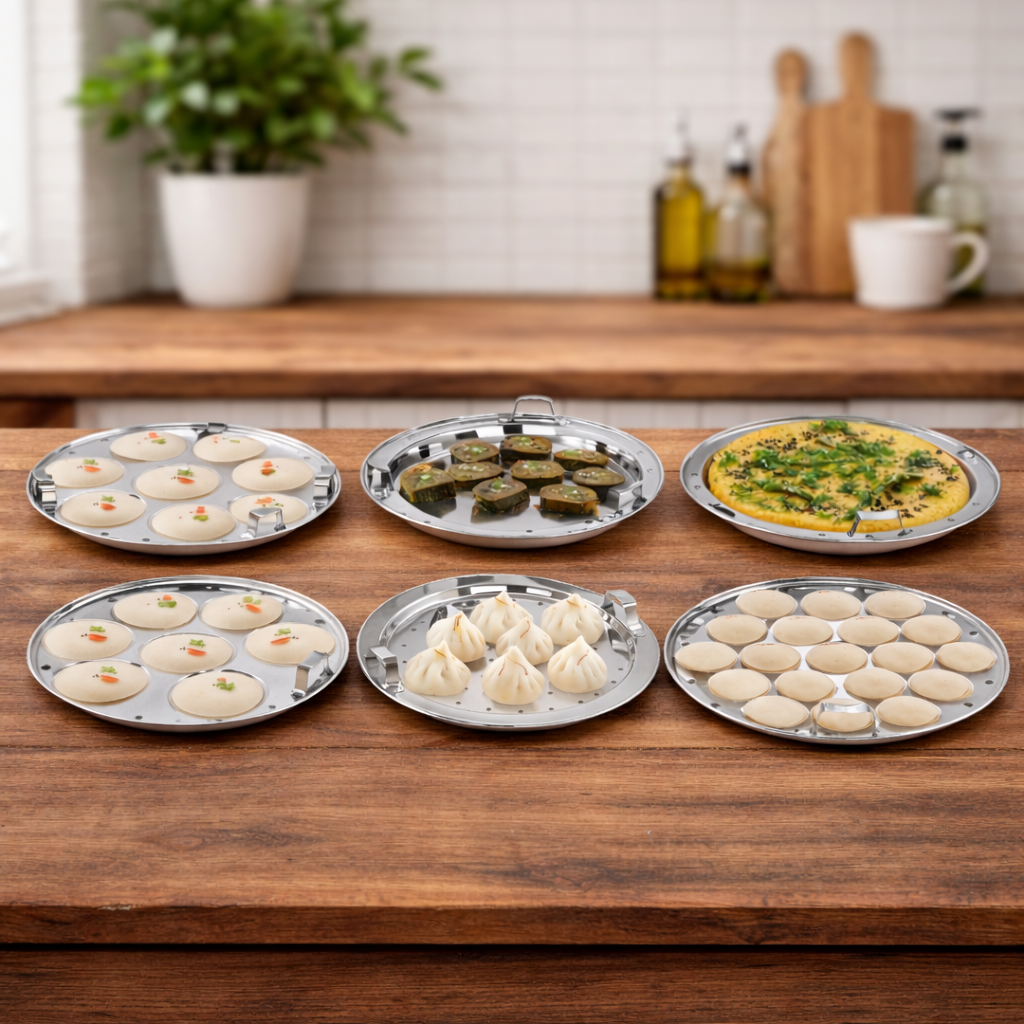 Stainless steel multi kadai plates with steamed idlis, dhokla, modak and momos on a wooden kitchen counter